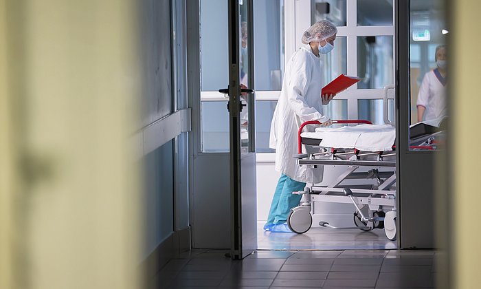 A hospital bed is pushed across a hospital corridor. 