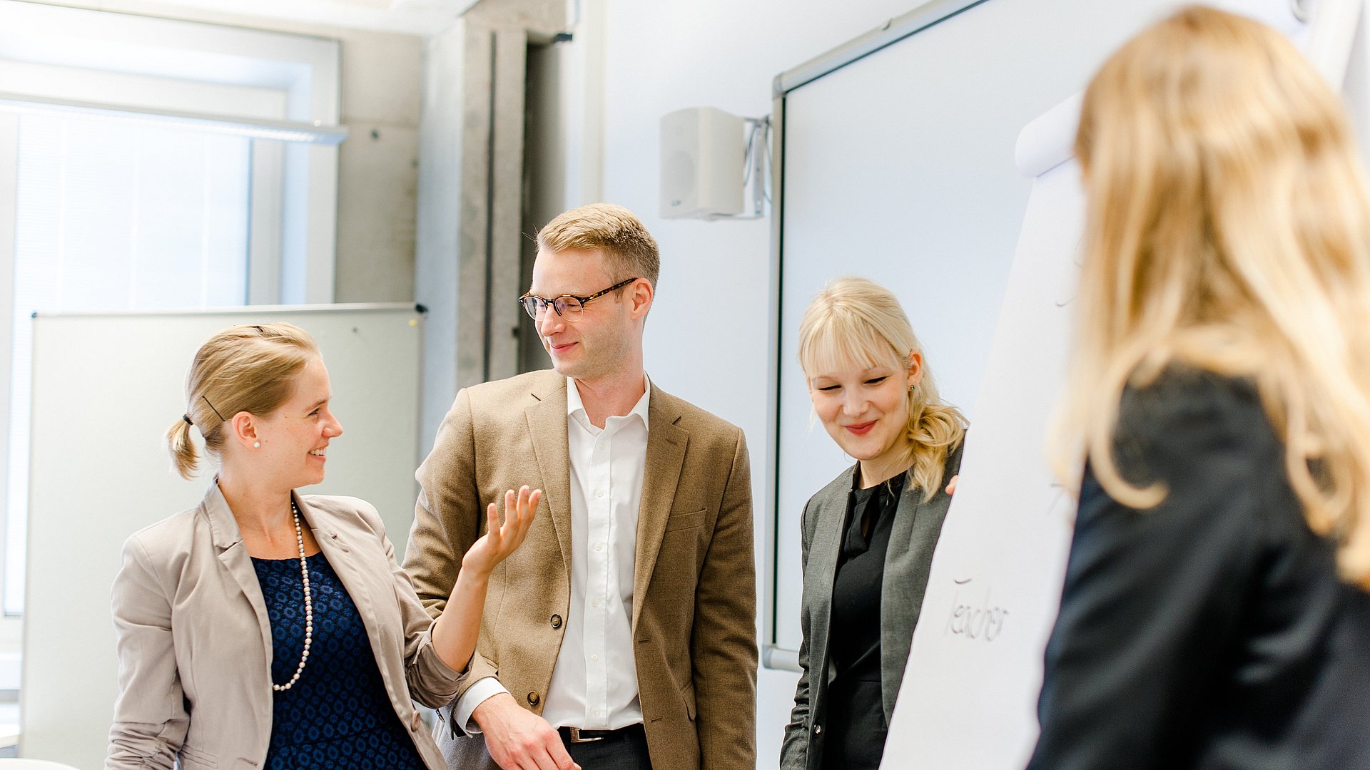 Drei Frauen und ein Mann stehen vor einem Flipchart und besprechen dich dazu.