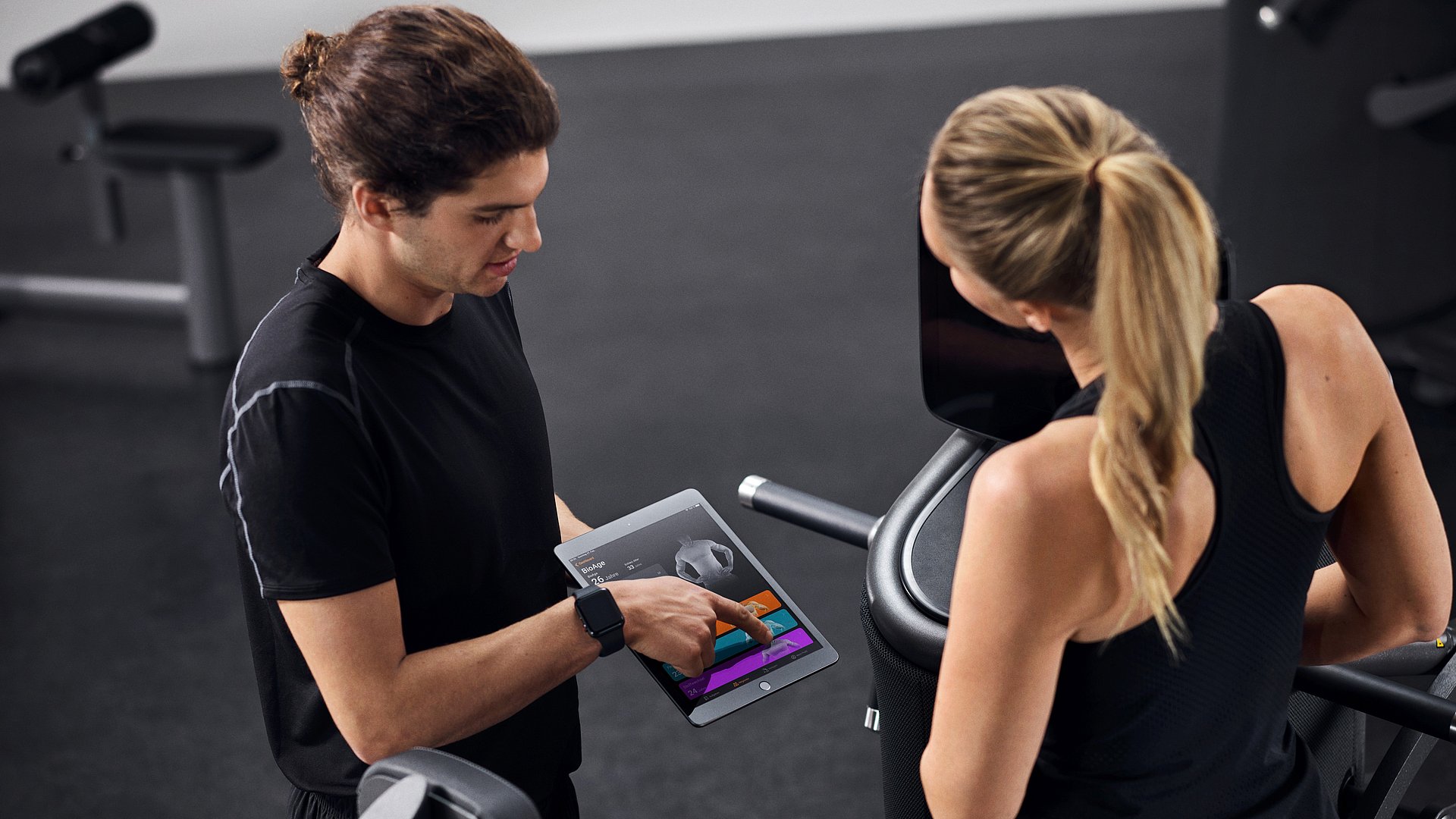 Ein Trainer bespricht anhand der EGYM-App das Trainingsprogramm mit einer Trainierenden.