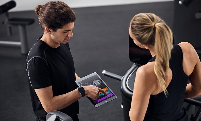 Ein Trainer bespricht anhand der EGYM-App das Trainingsprogramm mit einer Trainierenden.