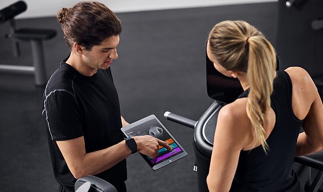 Ein Trainer bespricht anhand der EGYM-App das Trainingsprogramm mit einer Trainierenden.