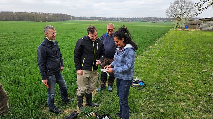Start-up NutriSen gets the laboratory on the field Eine Frau und drei Männer stehen auf einem Acker. Die Frau zeigt den Männern ein Gerät in ihrer Hand. Es handelt sich um das Gerät, dass das NutriSen-Team zur smarten Düngung entwickelt hat.