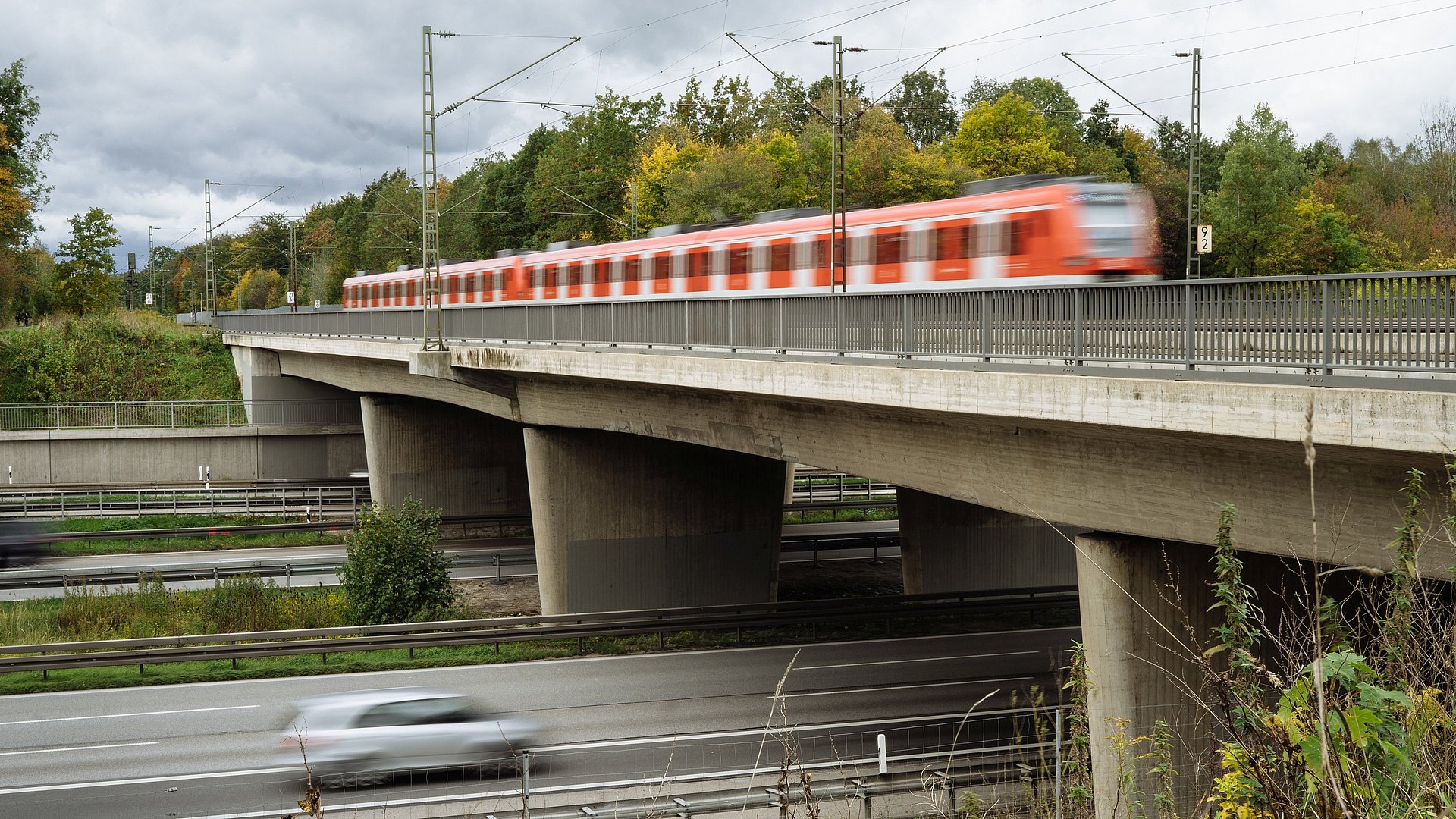 Foto zeigt eine Autobahnbrücke auf der gerade ein Zug vorbeifährt, darunter fährt ein Auto