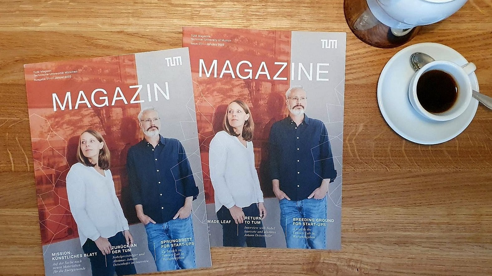  Two issues of the new magazine of the Technical University of Munich (TUM) on a wooden table, with coffee crockery next to it