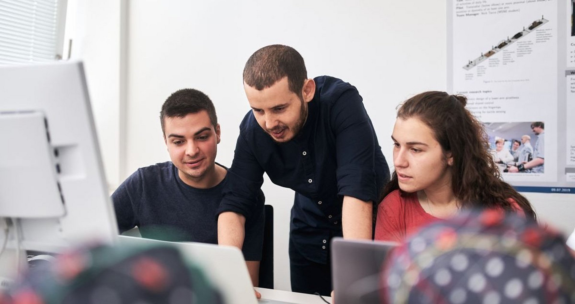 Two men and one woman in front of laptops talking.