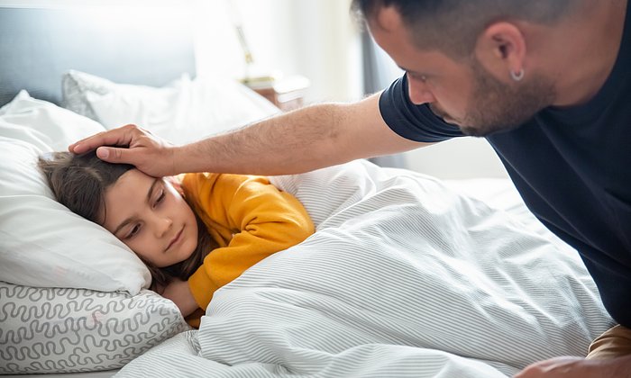 Ein krankes Kind in einem Bett wird von einem Erwachsenen getröstet