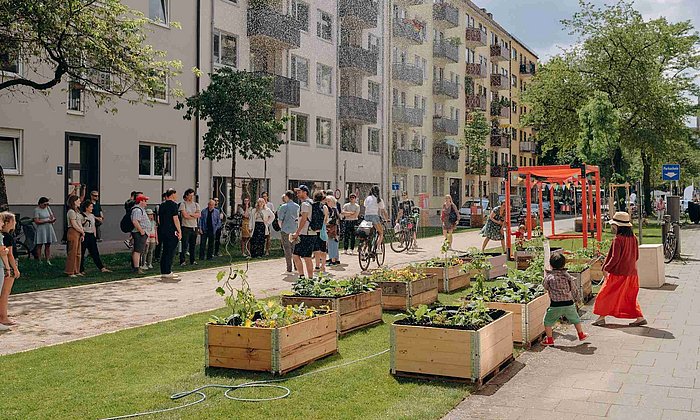 Menschen treffen sich in einem Münchner Straßenzug, der durch Pflanzenkästen begrünt wurde