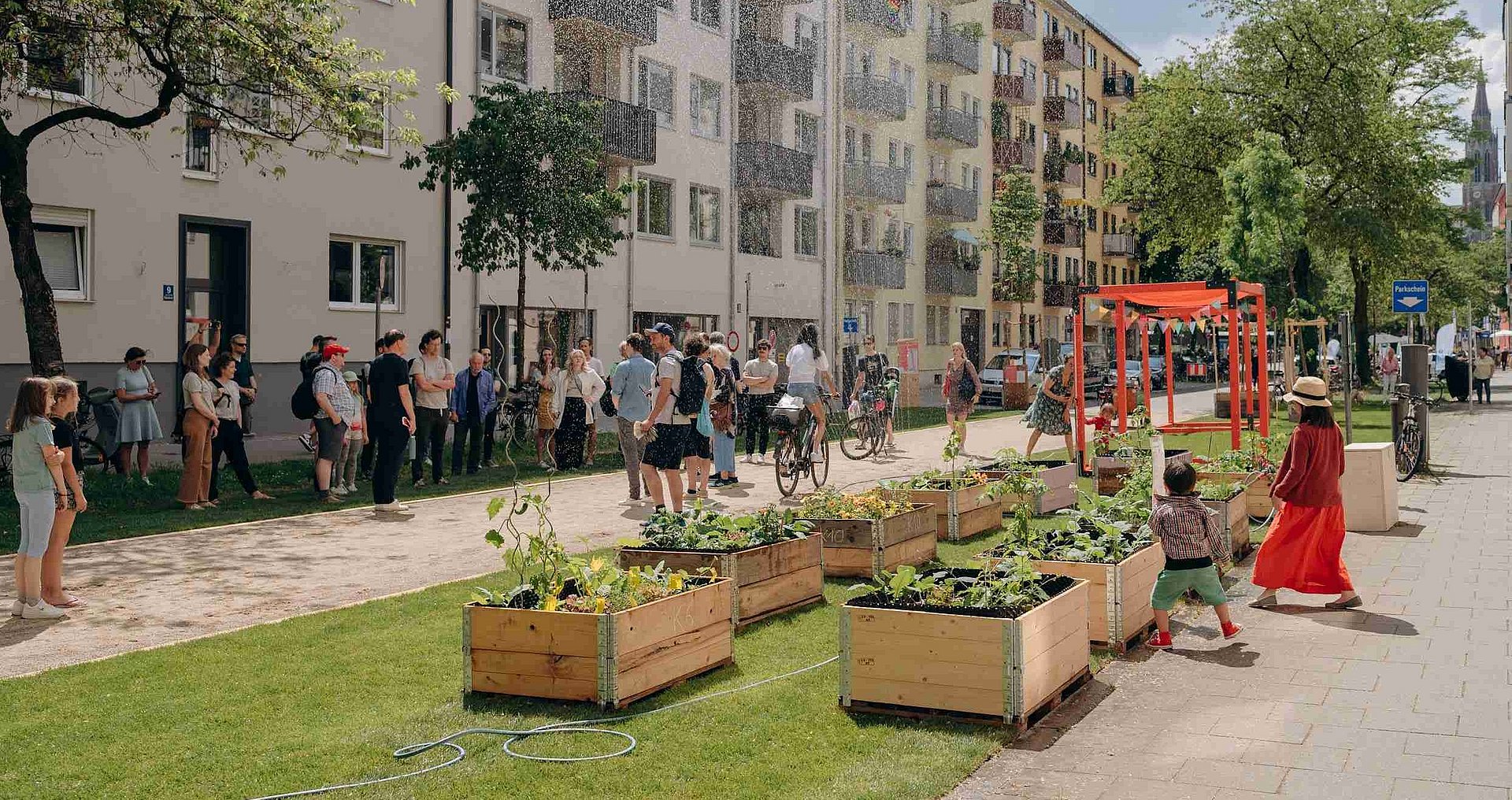 Menschen treffen sich in einem Münchner Straßenzug, der durch Pflanzenkästen begrünt wurde