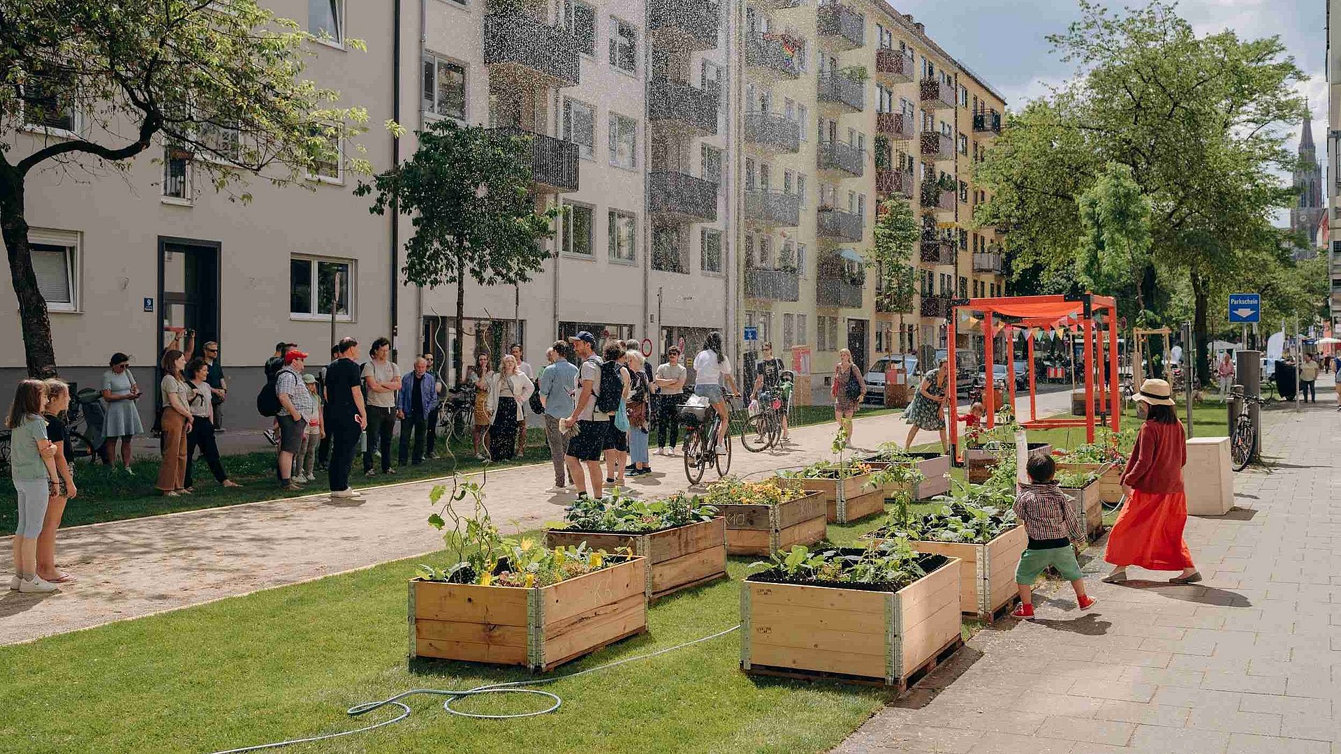 Menschen treffen sich in einem Münchner Straßenzug, der durch Pflanzenkästen begrünt wurde