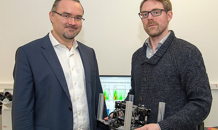 Prof. Dr. Juergen Hauer (left) and first author Erling Thyrhaug with their measuring instrument. In the background, spectra taken with it. (Image: A. Battenberg / TUM)