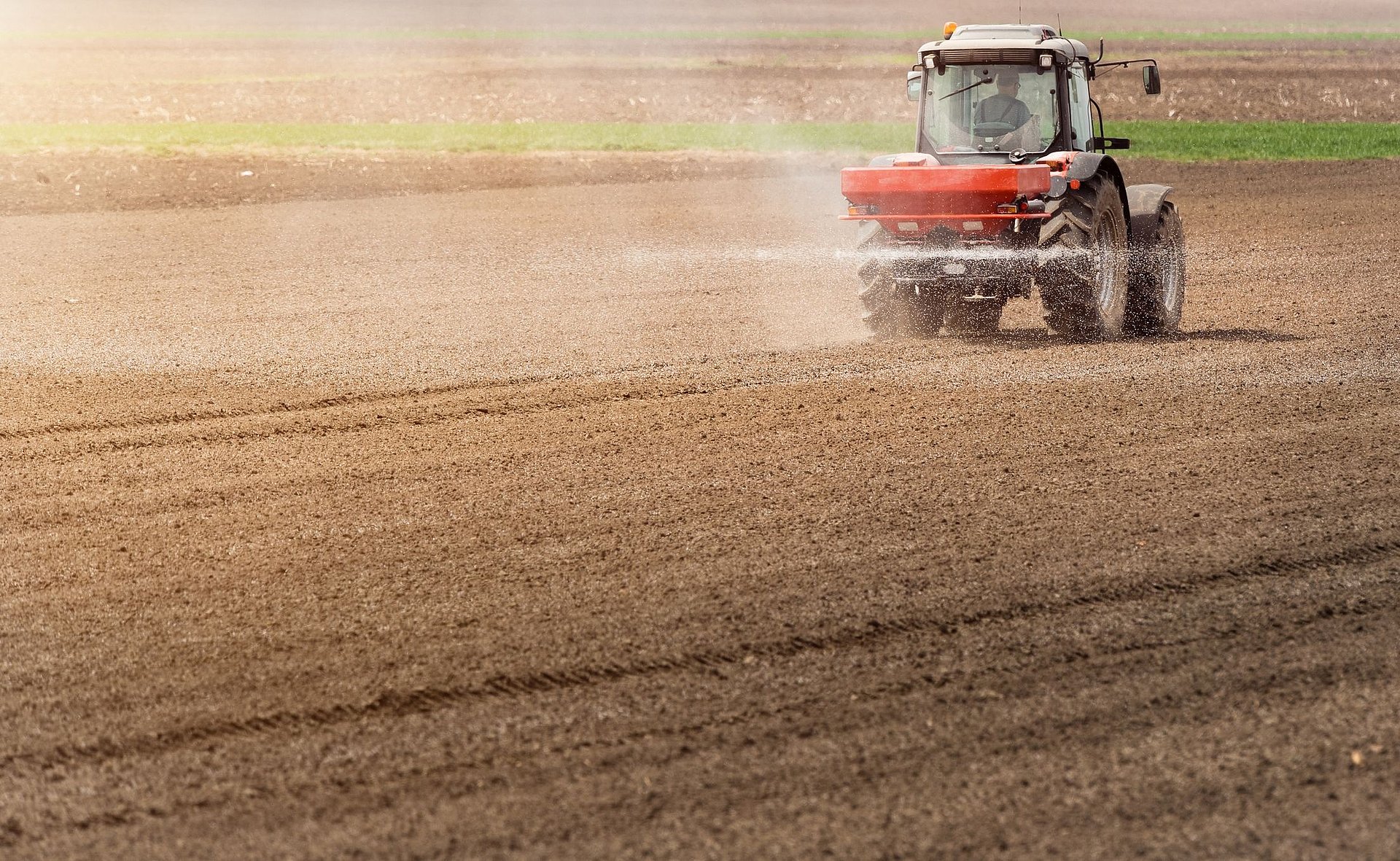 Ein Traktor fährt über einen Acker und trägt im Sprühnebel Stickstoff-Dünger auf.