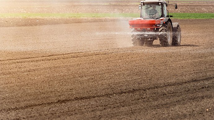 A tractor drives over a field and applies nitrogen fertilizer in a spray mist.