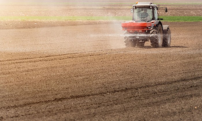 Ein Traktor fährt über einen Acker und trägt im Sprühnebel Stickstoff-Dünger auf.