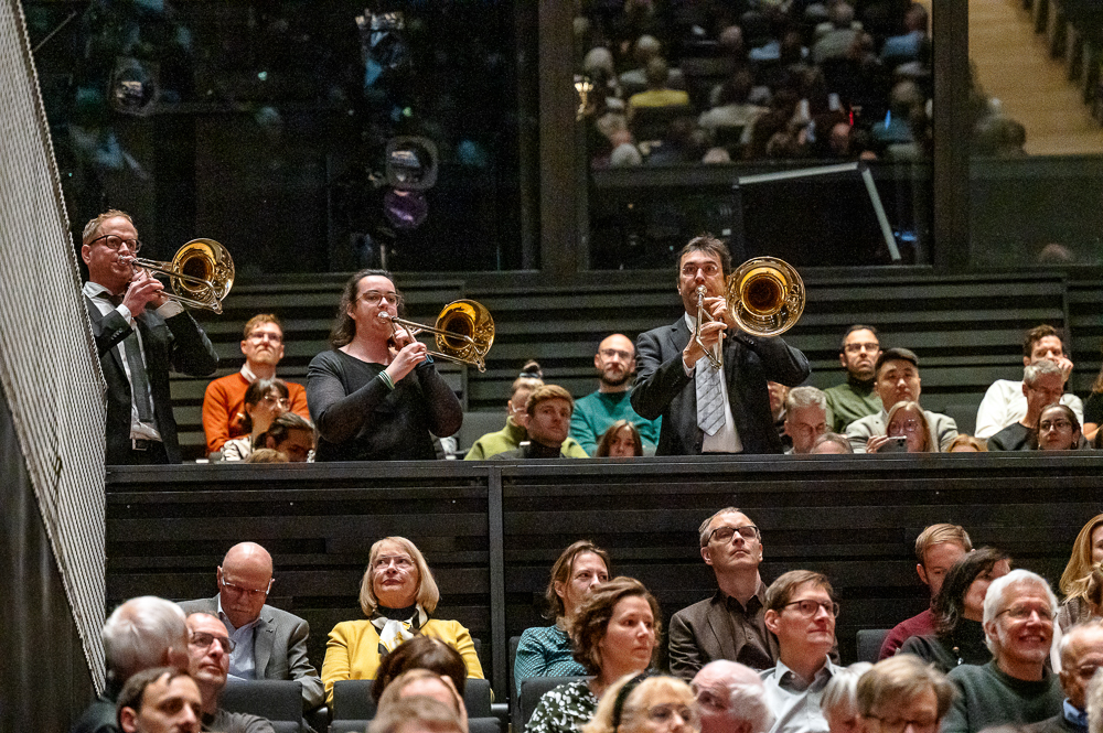 three trombonists stand in the audience and play a piece